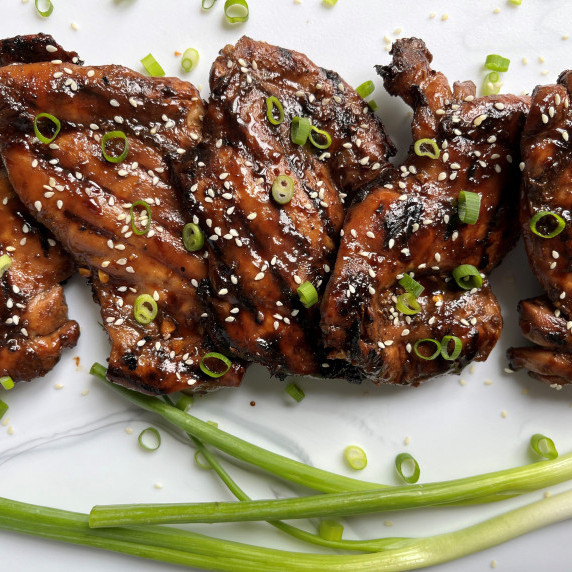 Balsamic marinated grilled chicken thighs on a marble board with green onion and sesame seeds.