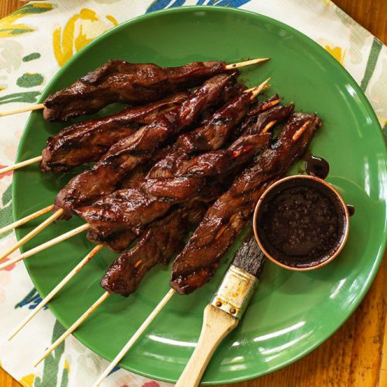 Grilled cherry teriyaki pork skewers on a green plate with a side of dipping sauce.