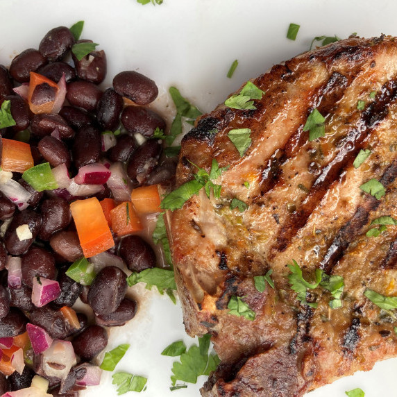 Grilled pork chop and black bean salad garnished with minced cilantro on a white plate.