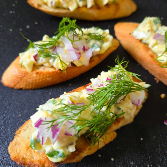 Golden crostini topped with creamy egg salad with pops of purple and green garnishes