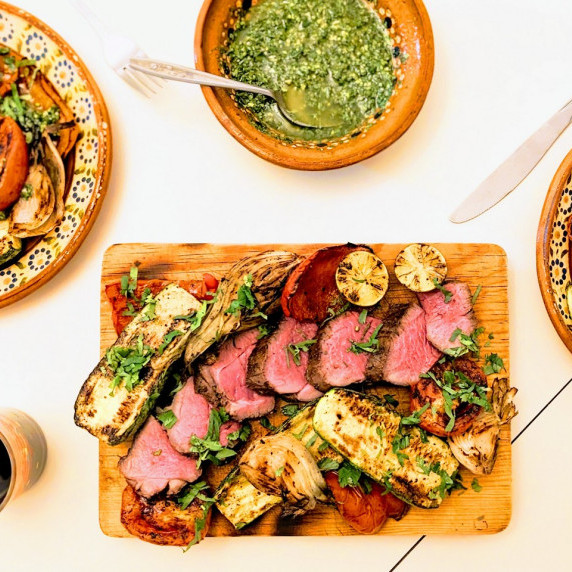 Grilled lamb and summer veggie platter on a table with fixings