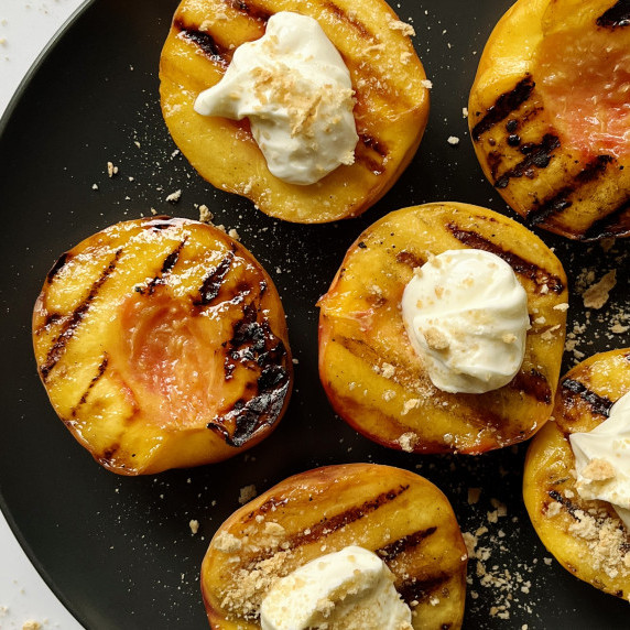 Grilled peach halves topping with a cream filling on a black plate.