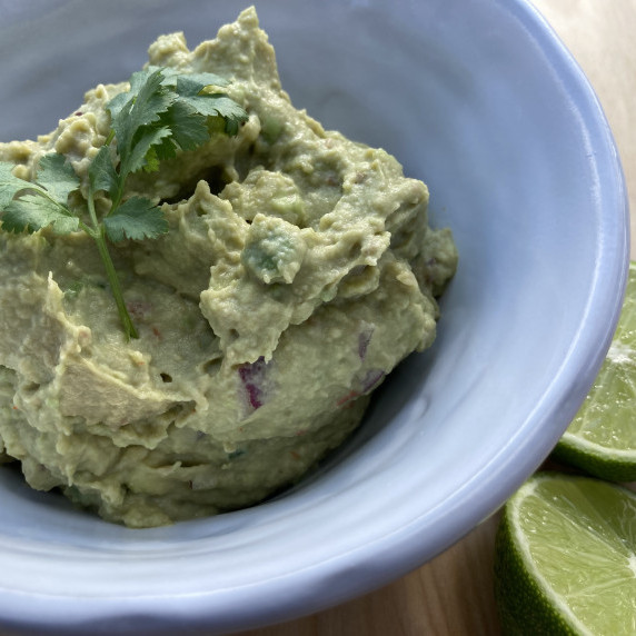 Guacamole in a white bowl garnished with cilantro and limes.