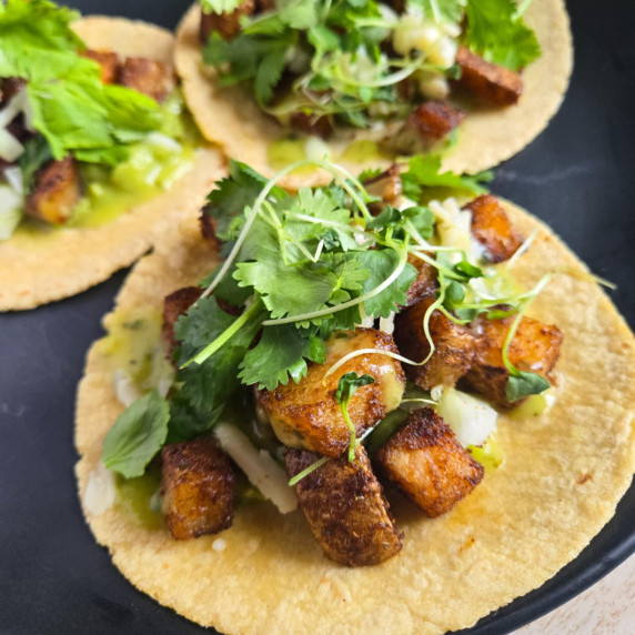 Yellow tortillas full of golden potatoes and green garnishes on a black plate.