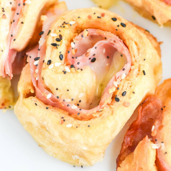 Ham and cheese pinwheel roll with sesame seeds on top, showing layers of ham and melted cheese.