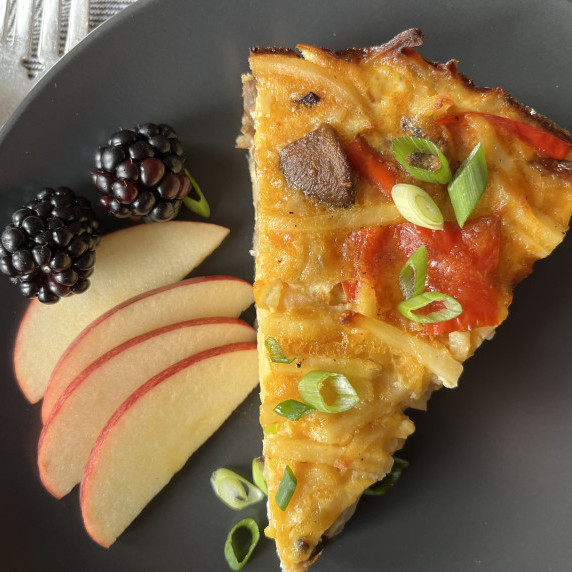 Hash brown casserole on a gray plate garnished with sliced apples and blackberries.