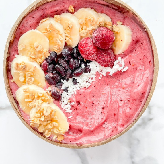 A pink smoothie bowl in a bowl with sliced banana, berries, and granola.