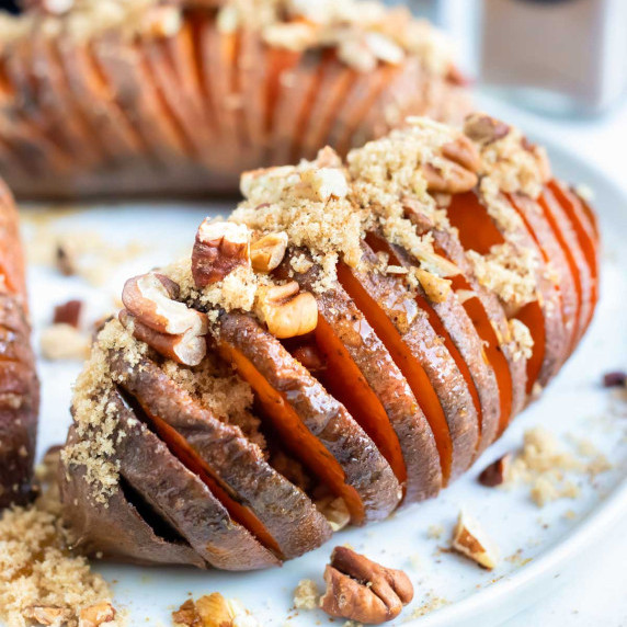 Hasselback Sweet Potatoes RECIPE served on a white dish topped with a pecan crumble.