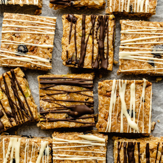 An array of no bake granola bars on parchment paper with chocolate drizzled on the top.
