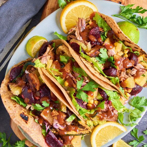 Plate of pulled pork tacos, filled with lettuce, coleslaw, sweetcorn, zucchinis and marinated beets.