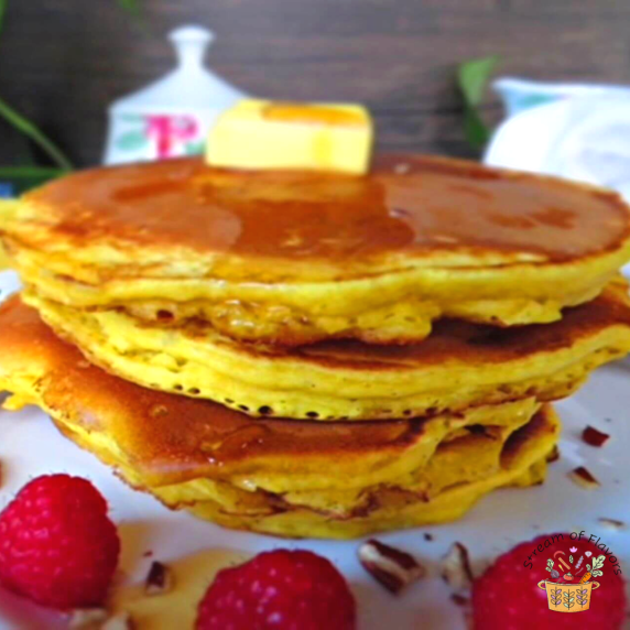 A stack of pumpkin pancakes with maple syrup and butter on a white plate with pecans and raspberries