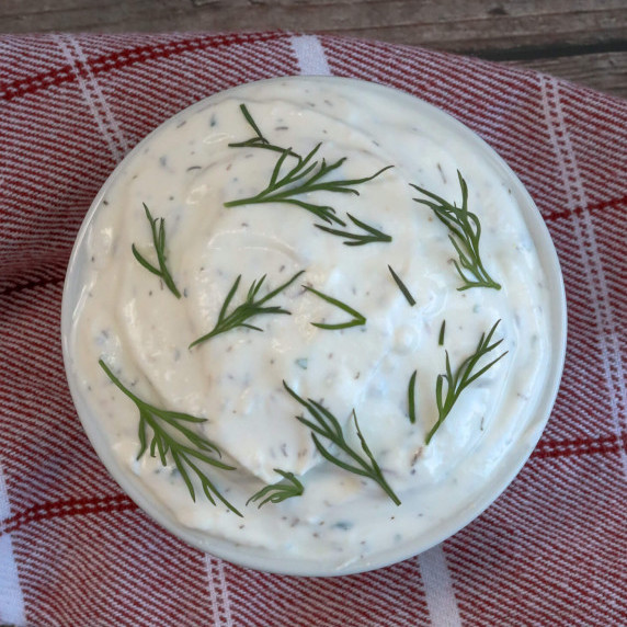 Top view of a small white dish of white dip covered in fresh dill