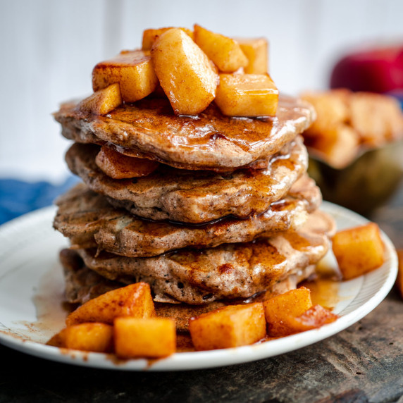 stack of fluffy apple buckwheat pancakes topped with diced maple apples on a white plate.