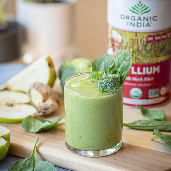 Green smoothie garnished with broccoli and spinach on a cutting board among ingredients.