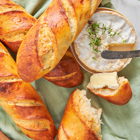 A few High Protein Sourdough Baguettes on a light green background, beside a camembert