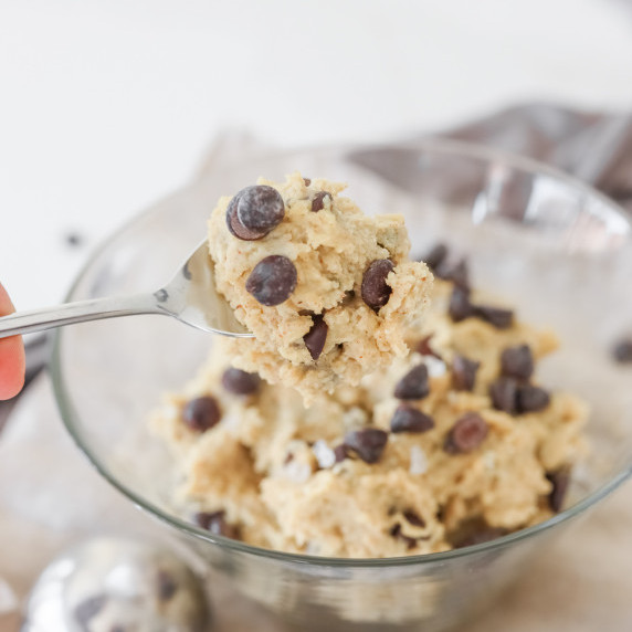 spoon taking scoop of edible cottage cheese cookie dough from clear glass bowl