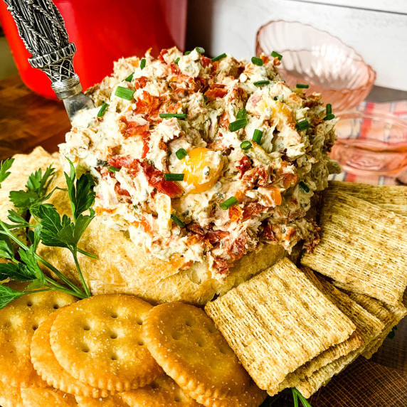 a serving platter with crackers and a hollowed out bread round filled with hoagie dip and red dutch 