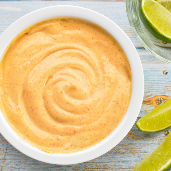 homemade chipotle mayo in a white bowl next to lime slices on a blue background
