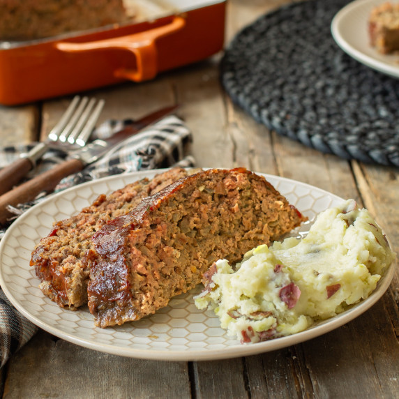Two slices of meatloaf with a side of mashed potatoes on a white plate.