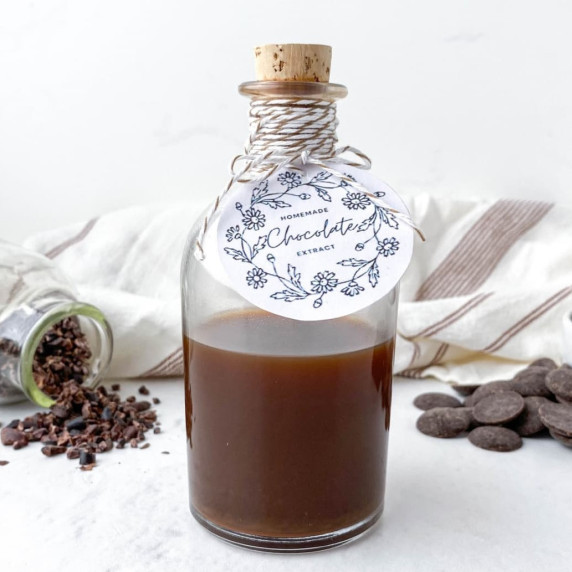 clear glass bottle with chocolate extract inside on a white background with chocolate nearby