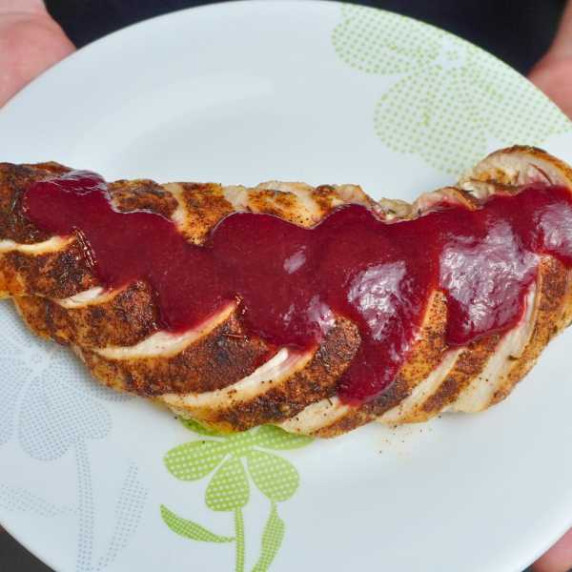 Homemade cranberry orange sauce spread on pieces of cooked turkey on a white plate. 