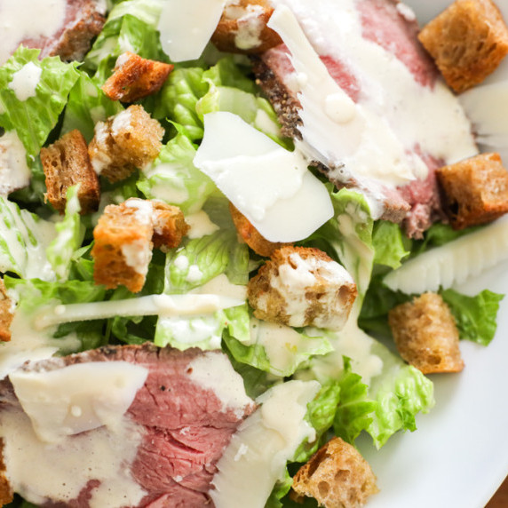 caesar salad dressing on a steak caesar salad with parmesan cheese and homemade sourdough croutons