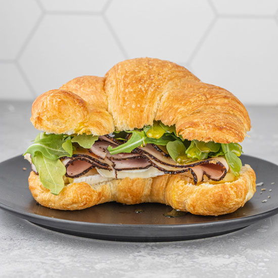 Pastrami Honey Brie Croissant Sandwich with arugula on Black small plate