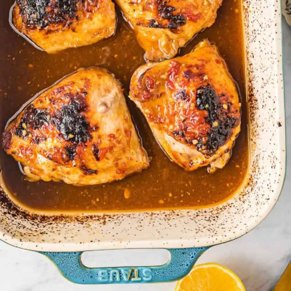 Close up of cooked chicken thighs in a honey garlic sauce in a baking pan from overhead