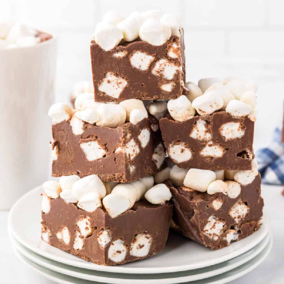 Hot chocolate fudge pieces full of mini marshmallows stacked high on a plate from the side.