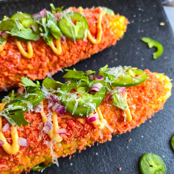 Gorgeous cob corn rolled in fiery red cheetos & garnished with green herbs, jalapenos, & red uns.