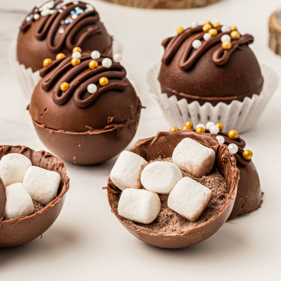 hot chocolate bombs with one open at the front showing the inside ingredients of marshmallows 