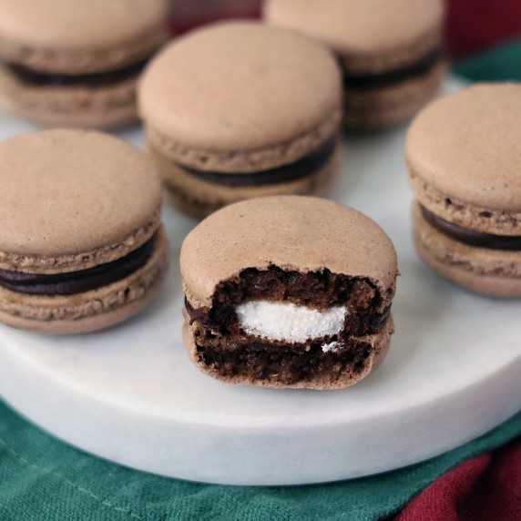 Hot cocoa macarons arranged on a snowman serving board, the front one with a bite out of it.
