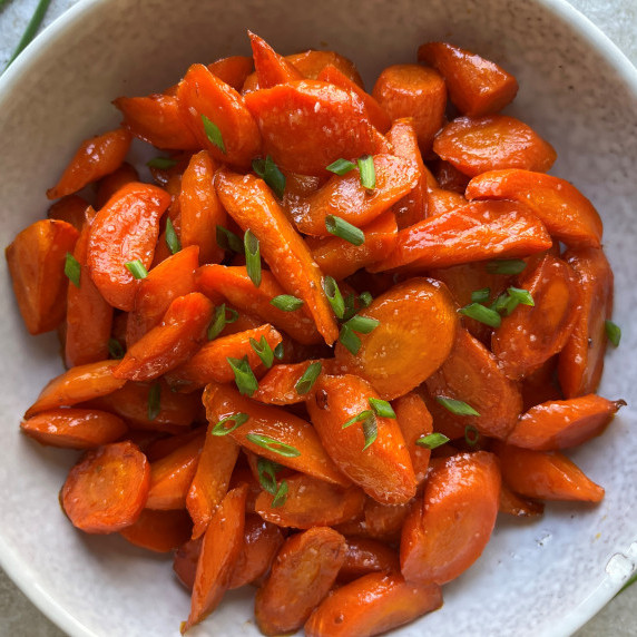 Hot honey roasted carrots topped with fresh minced chive in a white bowl.