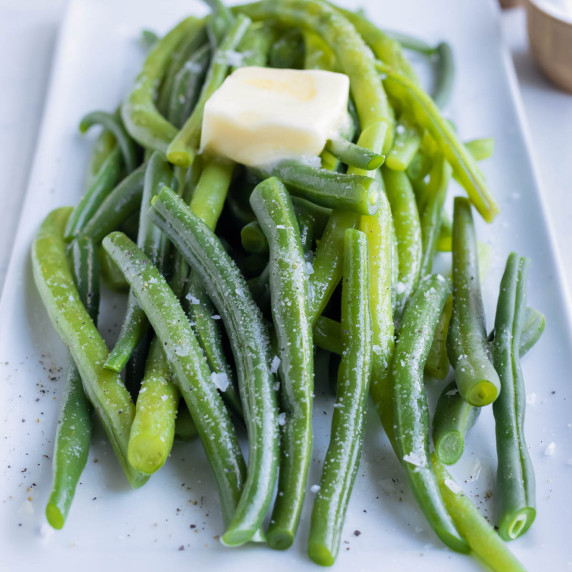How to Blanch Green Beans RECIPE placed on a white platter topped with salt and butter.