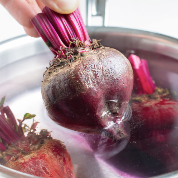 How to Boil Beets RECIPE with a beet halfway out of a pot full of water and beets.