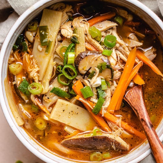 Hot and sour soup, chicken, bamboo shoots, mushrooms, scallions and wooden spoon in a white bowl