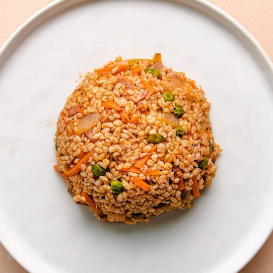 Fried shirataki rice with peas and carrots in an oval on a white plate