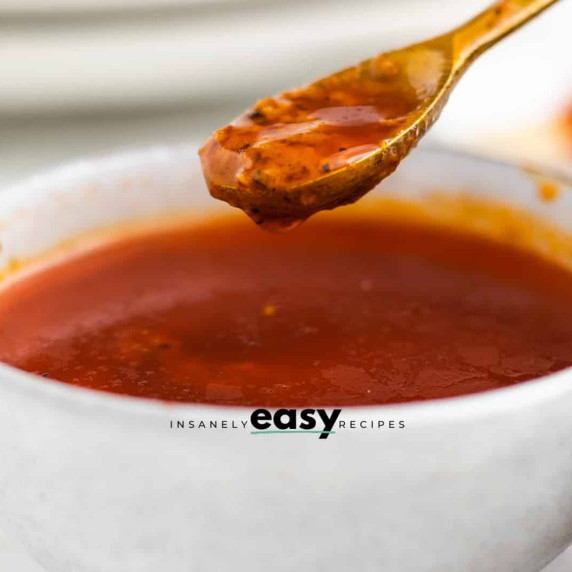 Flavorful red sauce in a white bowl, a spoon scooping some out