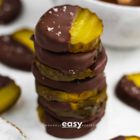 Stack of chocolate covered pickles on a white surface, some pieces nearby