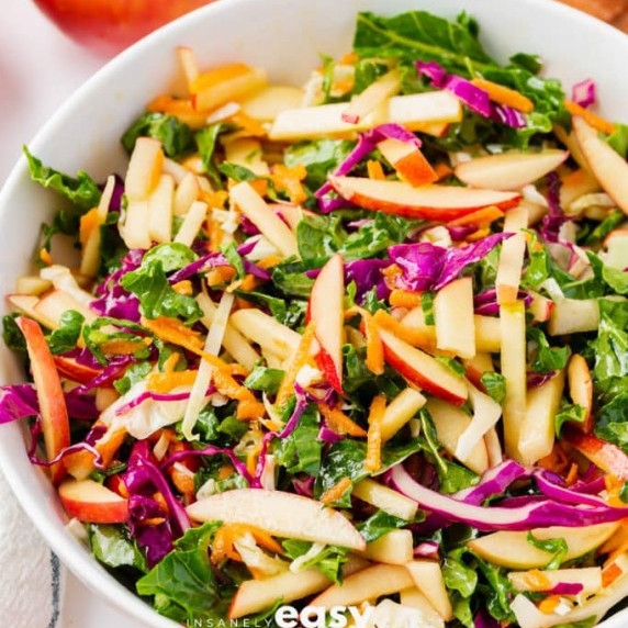 Coleslaw made of shredded kale, apple, red and green cabbage, and carrots in a white bowl