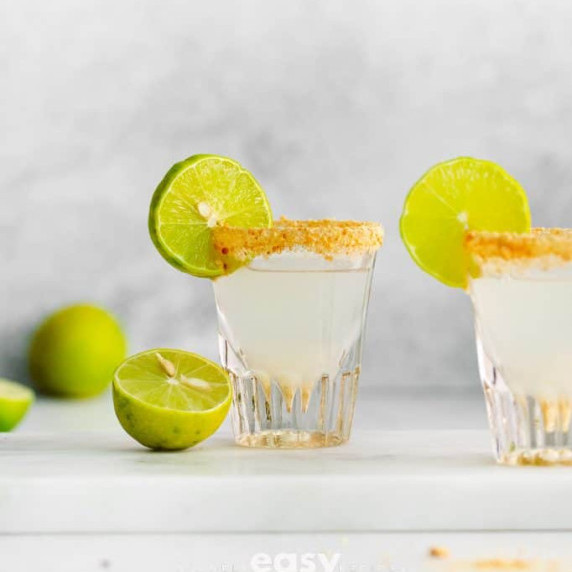 Two glasses of lime pie shot garnished with lime slices and crushed biscuit rim