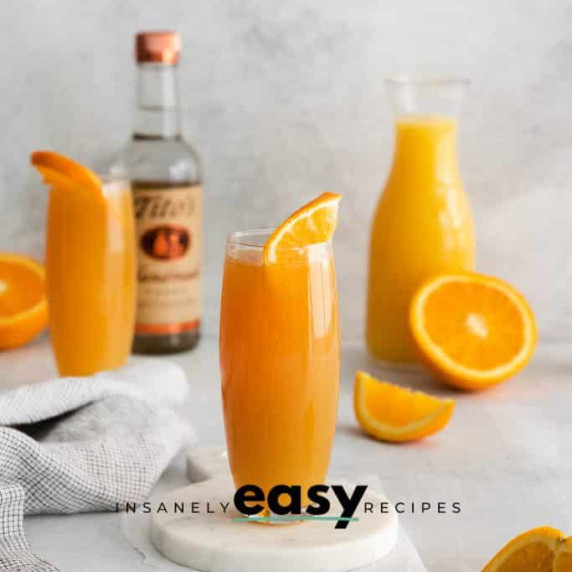 Glasses and a pitcher of manmosa with orange wheel as garnish, a bottle of vodka at the back 