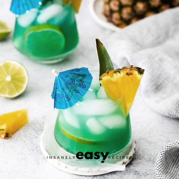 Glasses of iced blue green mermaid water with a pineapple wedge on the rim and a cocktail umbrella