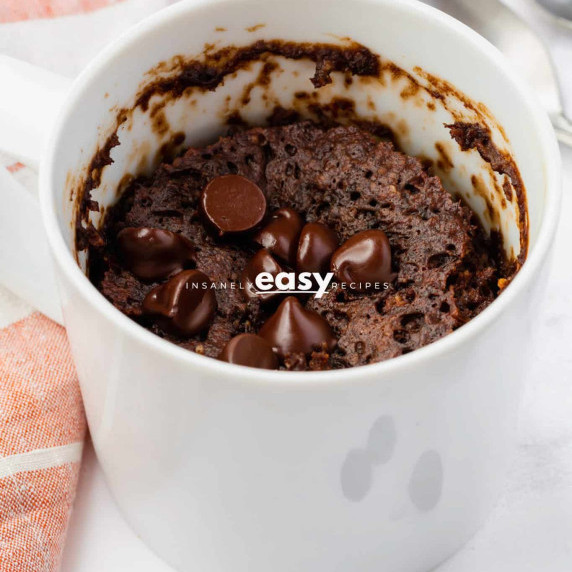 Chocolate protein mug cake topped with chocolate chips in a white mug