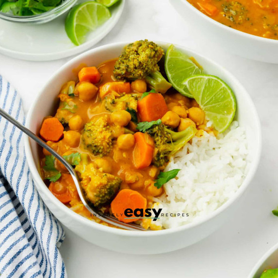 Pumpkin curry served with rice and lime slices in a white bowl with a fork, a dish towel next to it