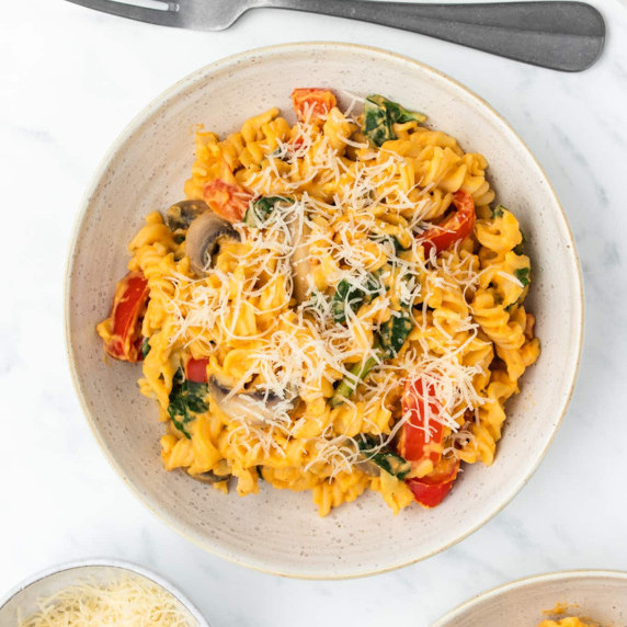 Fusilli pasta with sweet potato sauce, mushroom, & red peppers, topped with grated cheese on a plate