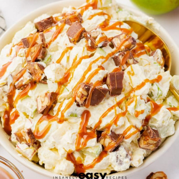 Snicker apple salad with diced snicker bars and caramel sauce drizzle in a white bowl 