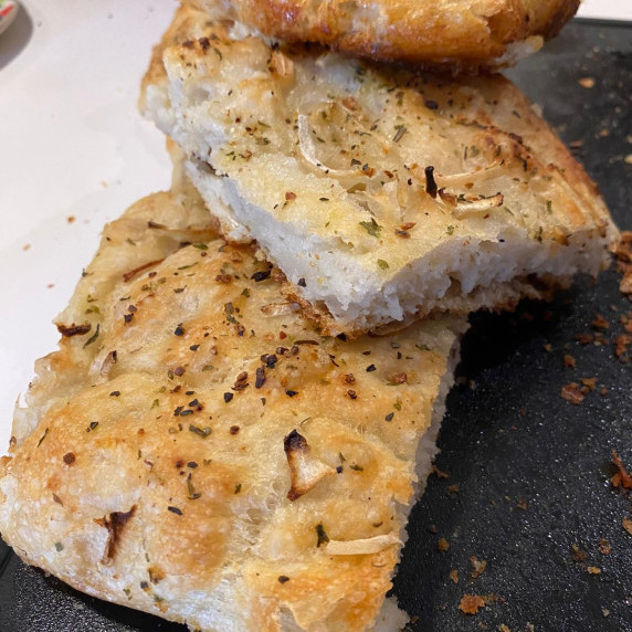 A close-up view of a freshly baked focaccia bread, sliced and seasoned with herbs and spices.