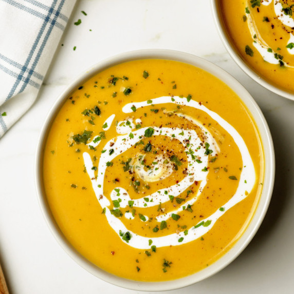 A white bowl with pumpkin soup with coconut cream