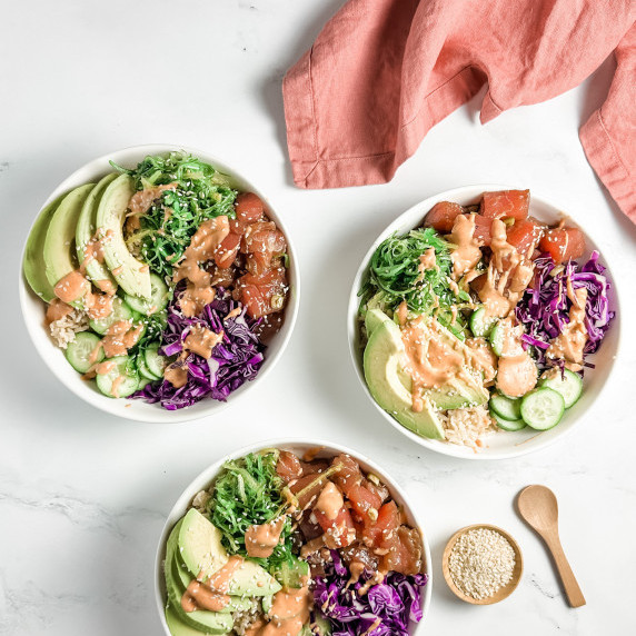 Tuna poke bowls with fresh ground ginger on a counter dressed with cucumber, cabbage, and avocado